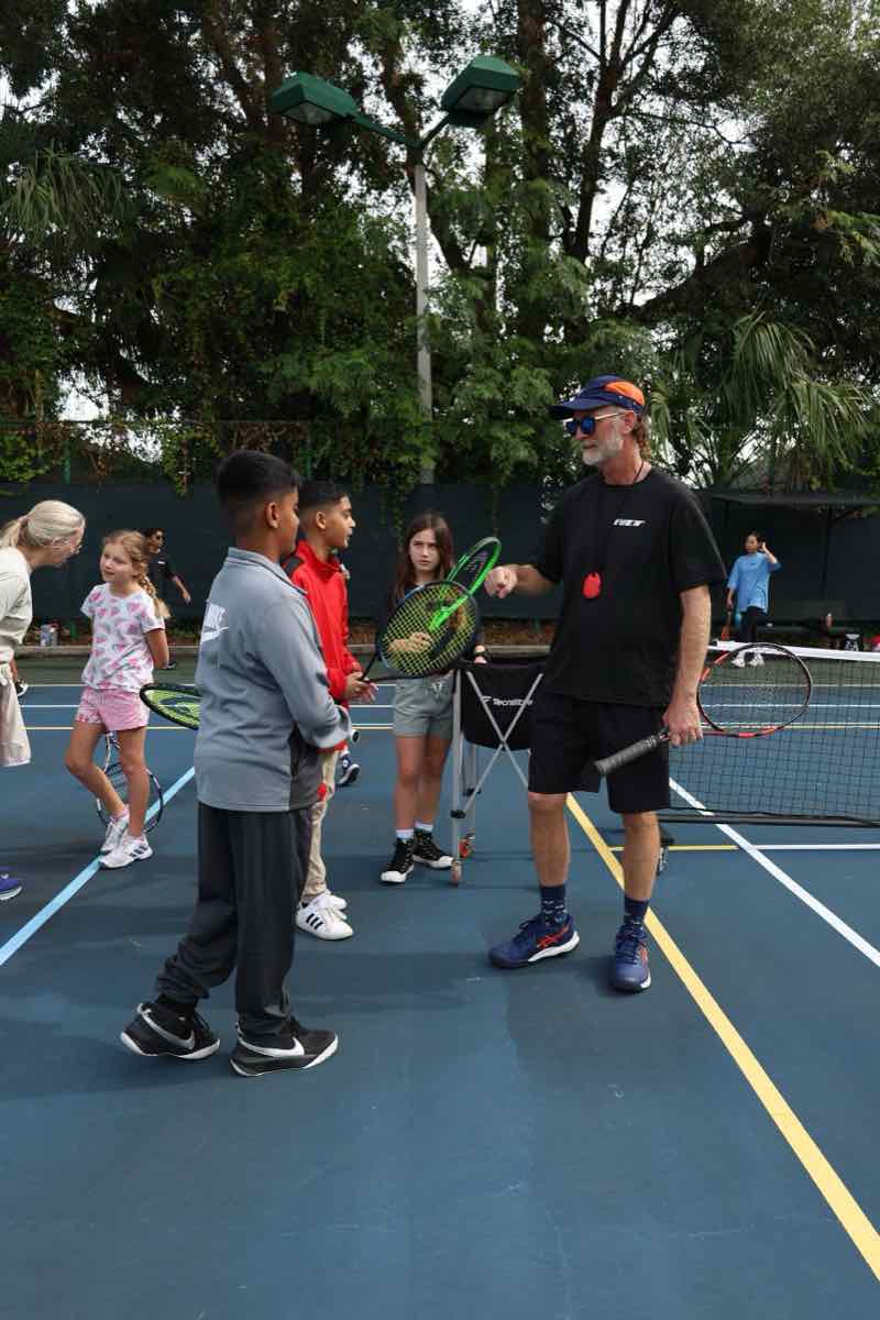 A coach giving instruction to a group of junior players on court